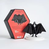 A collectible art toy figurine of a vampire with outstretched cape wings, standing on a white circular base next to its black and red packaging box.