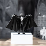 Vampire figurine with a cape on a white pedestal against a blurred background