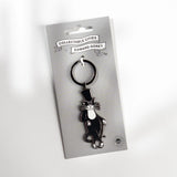 A black and white enamel keychain shaped like a cat wearing a top hat, attached to a silver key ring and displayed on a branded silver backing card. The card reads 'Collectable Cities x Edward Gorey'.