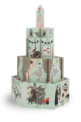 A vintage-style illustrated paper tower set on a plain white background. The tower is made of multiple printed paper panels with whimsical drawings