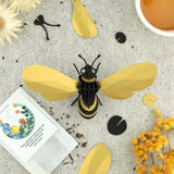 Decorative bee sculpture on a textured surface with flowers and a book.