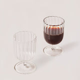 A set of two clear glass stemware items with a striped pattern on a plain background.