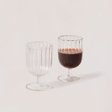 A set of two clear glass stemware items with a striped pattern on a plain background.