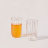 Two clear glass tumblers with a striped pattern, one with a liquid inside, the other is empty.