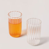 Two clear glass tumblers with a striped pattern, one with a liquid inside, the other is empty.