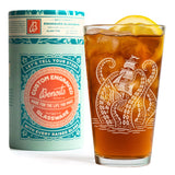 A custom engraved glass with an octopus design and a lemon garnish, shown next to its mint green and orange branded Benoit's glassware packaging on a white background.