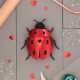 Red ladybug-shaped container with black spots on a gray surface with heart decorations.