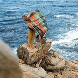 Person wrapped in a colorful blanket standing on rocks by the ocean