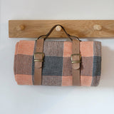 Woven bag with leather straps hanging on a wooden rack against a white wall.