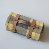 Roll-up picnic blanket with brown straps on a light gray background