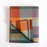 Folded fabric with a checkered pattern in orange, gray, and green on a white background