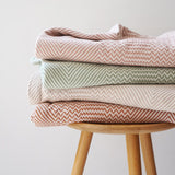 Stack of patterned blankets on a wooden stool against a plain background