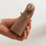 A hand holding a small wooden bottle opener shaped like the character No-Face from Spirited Away, photographed against a plain light background.