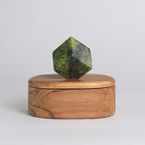 An oval-shaped wooden jewel box with a stone geometric handle on top, placed on a plain background.