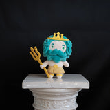 A plush toy character resembling a sea king, with turquoise blue curly hair and beard, a white face and body, a yellow crown, and a yellow trident, standing on a white surface against a dark background.