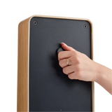 A close-up of a hand with a gold ring turning a black dial on the back of a wooden electronic device, shown against a plain white background.