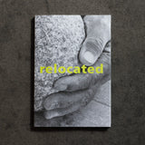 A book cover featuring a black-and-white close-up of a hand resting on a rough stone, with the word 'relocated' in bright yellow across the center, displayed against a dark textured background.
