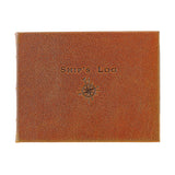 A rectangular brown textured leather book or journal cover with 'SHIP'S LOG' embossed at the top and a compass rose design below, shown on a plain white background.