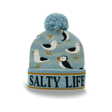 A light blue knit beanie with a fluffy pom-pom on top, featuring a pattern of seagulls and the words 'SALTY LIFE' on the cuff.