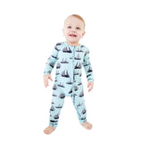 A baby standing and smiling while wearing a light blue footed zip-up sleeper with a black sailboat pattern, set against a plain white background.