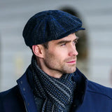 Man wearing a grey and blue checkered flat cap and scarf against a blurred background
