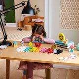 Child playing with colorful building blocks at a desk in a room with a lamp and books.