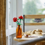 Brown glass bottle with red flowers on a wooden table by a window