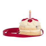 A plush cake-shaped shoulder bag with cream-colored faux frosting, red berry details, a candle on top, and a red strap, shown on a plain white background.