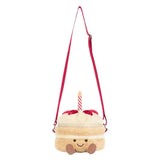 A plush crossbody bag designed like a cute frosted cake with a single candle on top, featuring a red strap and a smiling face on the front, set against a plain white background.