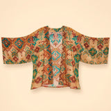 A lightweight open-front kimono jacket with wide sleeves, featuring a colorful geometric and tribal-inspired pattern in brown, teal, orange, and beige on a warm cream background.