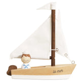 A wooden toy sailboat with white sails, a brown mast, a small painted sailor figure, and the words 'la mer' on the side, shown on a plain white background.