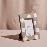 A concrete picture frame with white marble inlay, standing on a beige surface, with a brand tag in the center.