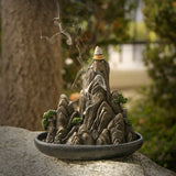 Decorative incense burner shaped like a mountain with smoke rising, placed outdoors.