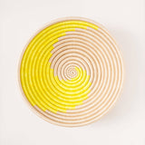 Round woven basket with yellow and beige spiral pattern on a white background