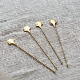 Set of four gold stirrers with shell designs on a textured gray surface