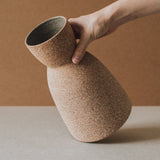 A conical ceramic vase with a textured, earthy finish on a neutral background.