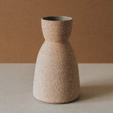 A conical ceramic vase with a textured, earthy finish on a neutral background.