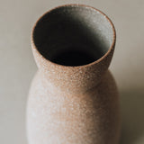 A conical ceramic vase with a textured, earthy finish on a neutral background.