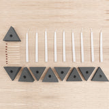A candle kit laid out on a light wood surface, including black triangular candle holders, white taper candles, and a matches.
