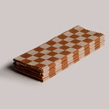Four folded and stacked woven placemats in a checker board pattern of orange and tan.
