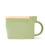 A square ceramic salt box in sage green with a hinged wooden lid, shown on a clean white background.