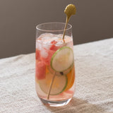 Glass of iced cocktail with fruit and a gold stirrer on a textured surface