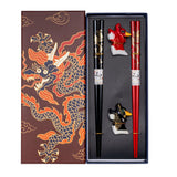 A gift set of chopsticks and rests with a gold dragon design on a red and black background, displayed in a box with a matching design.
