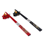 A gift set of chopsticks and rests with a gold dragon design on a red and black background.
