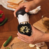 Person using a garlic crusher on a wooden surface with ingredients around