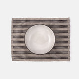 A placemat with a geometric pattern, predominantly in black and white, under a white dinner plate.