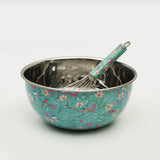 Floral-patterned metal mixing bowl with a whisk on a white background