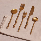 Set of five wavy handled utensils in a brushed brass finish.