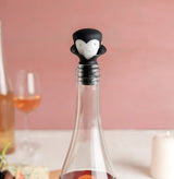 Wine bottle stopper with a character design on a table with wine glasses and food.