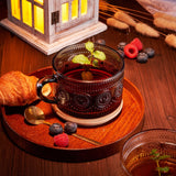 Glass mug with tea on a wooden tray with berries and a candle in the background
